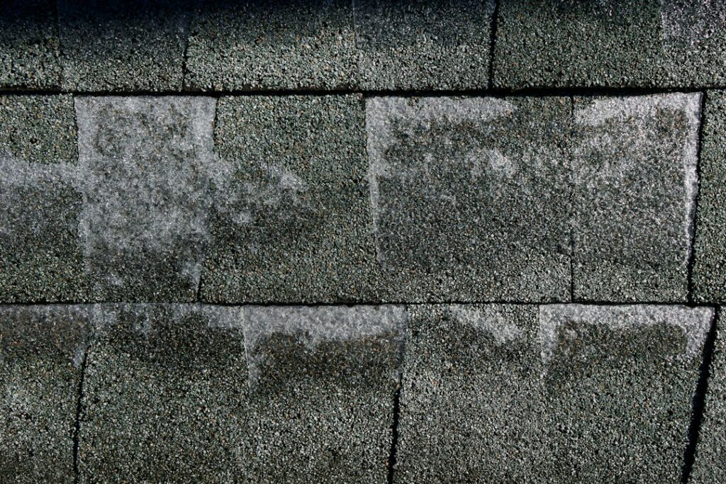 Homeowner examines bruised asphalt shingles and dented metal flashing after a hailstorm.